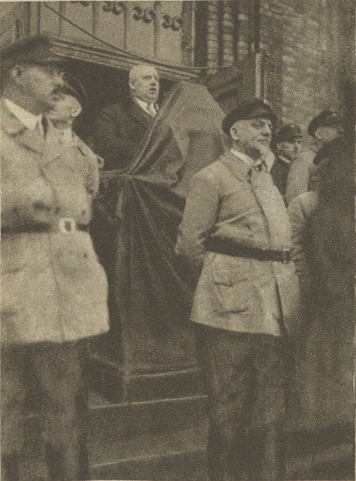 Historisches Schwarz-Weiß-Foto: Heinrich Hirtsiefer steht an einem Rednerpult, das von Reichsbanner-Männern mit Schirmmütze geschützt wird.