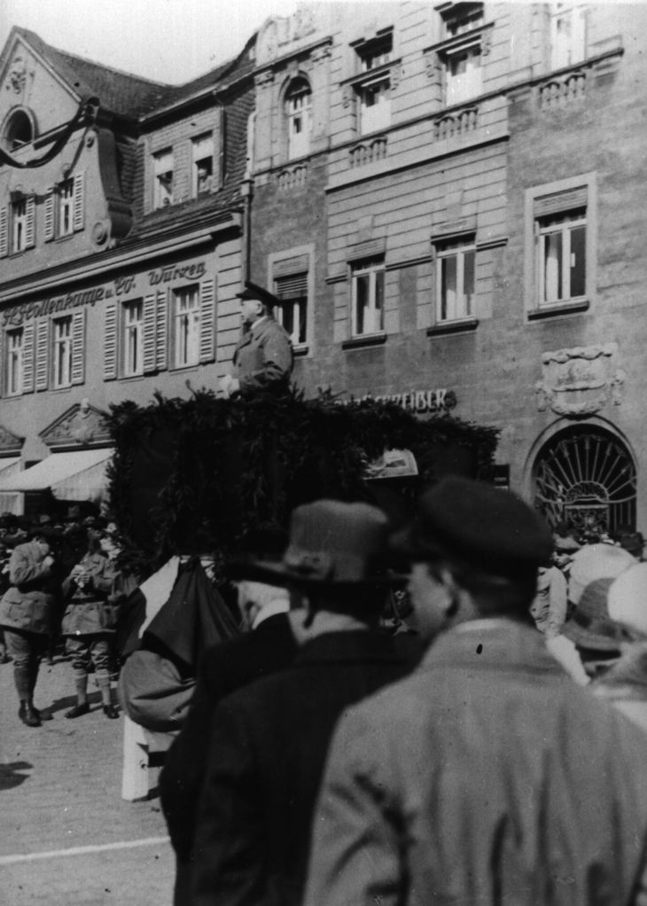 Historisches Schwarz-Weiß-Foto: Richard Lipinski steht auf einer Rednerbühne vor mehrstöckigen Wohnhäusern.